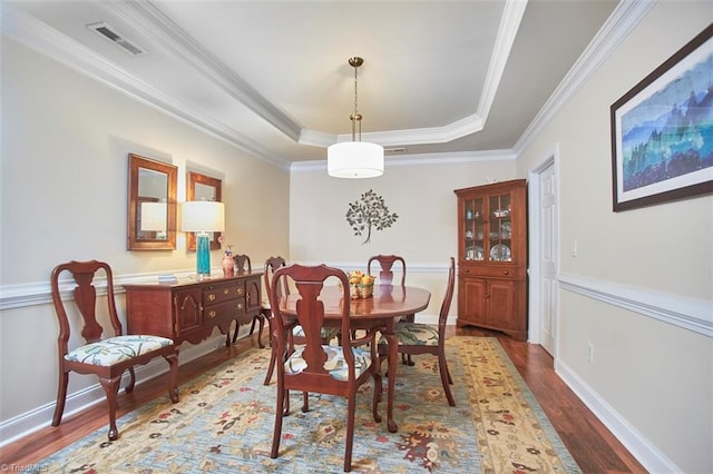 dining room with wood finished floors, visible vents, baseboards, a tray ceiling, and crown molding