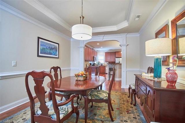 dining area featuring visible vents, arched walkways, a raised ceiling, and wood finished floors