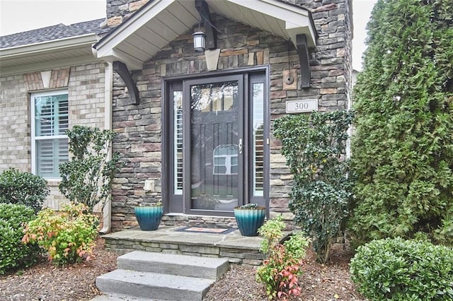 doorway to property with stone siding, a chimney, and a shingled roof