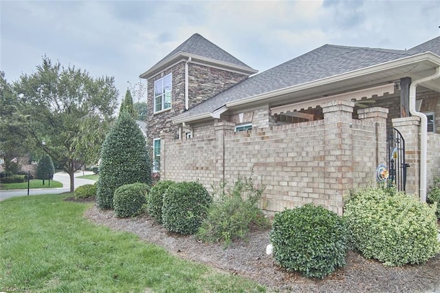 view of side of property with brick siding, stone siding, a lawn, and roof with shingles