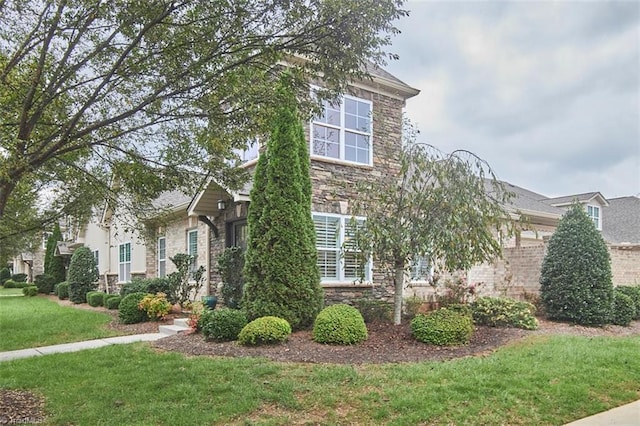 view of property hidden behind natural elements featuring a front lawn and stone siding