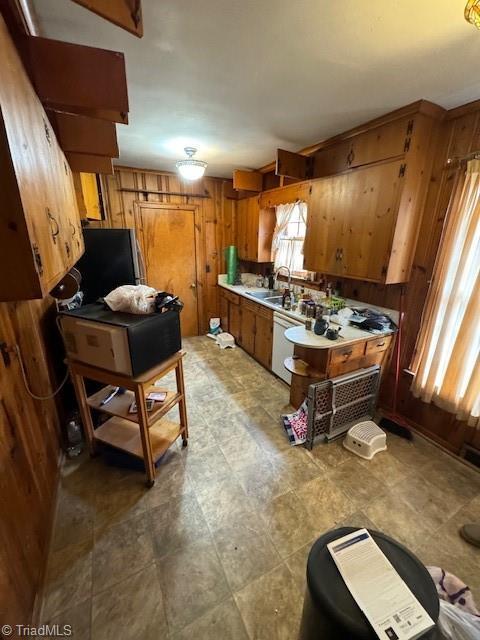 kitchen with sink, dishwasher, and wood walls