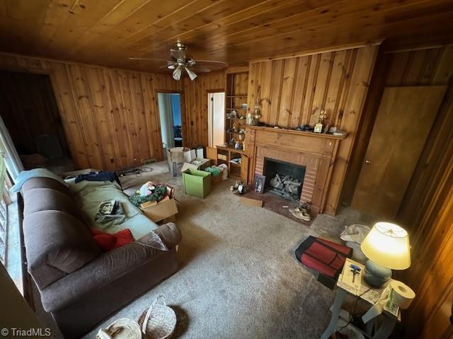 living room featuring wood walls, carpet floors, ceiling fan, wood ceiling, and a brick fireplace