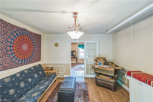 living room with a textured ceiling, wood finished floors, french doors, and wainscoting