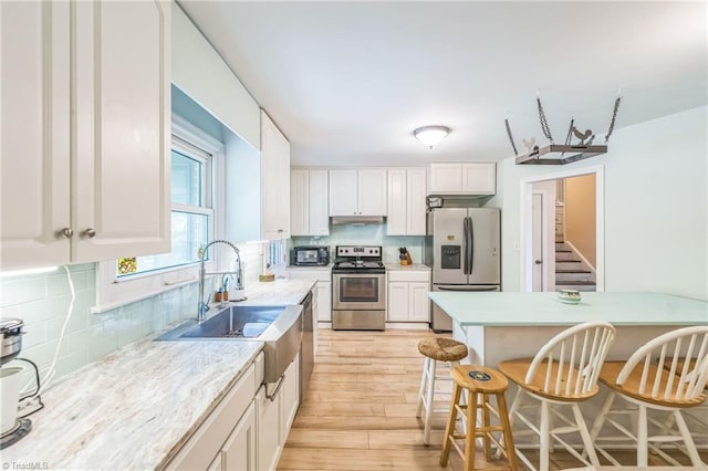 kitchen with stainless steel appliances, under cabinet range hood, a kitchen bar, white cabinets, and backsplash