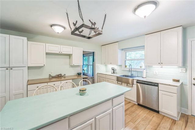 kitchen featuring stainless steel dishwasher, a sink, white cabinetry, decorative backsplash, and light countertops