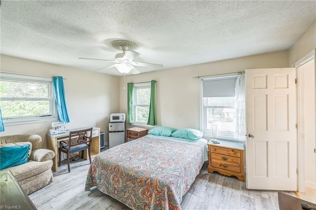 bedroom featuring multiple windows, wood finished floors, a textured ceiling, and ceiling fan