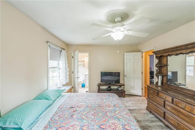 bedroom featuring light wood-style flooring, a textured ceiling, a ceiling fan, and connected bathroom