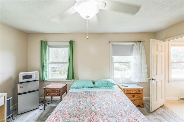 bedroom featuring fridge, wood finished floors, a textured ceiling, a ceiling fan, and baseboards