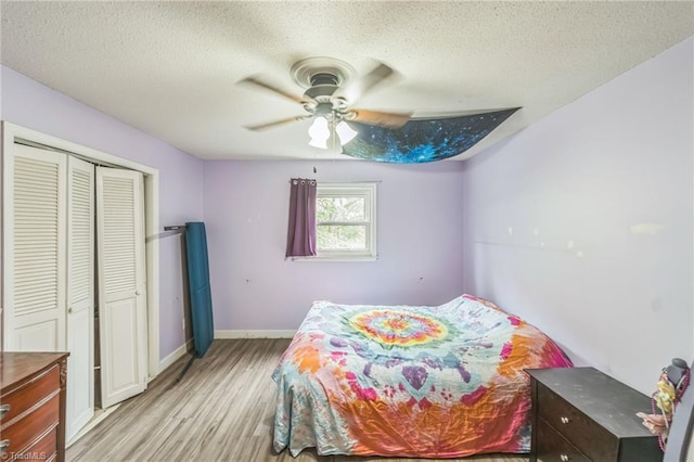 bedroom with light wood-style flooring, a textured ceiling, a closet, baseboards, and ceiling fan