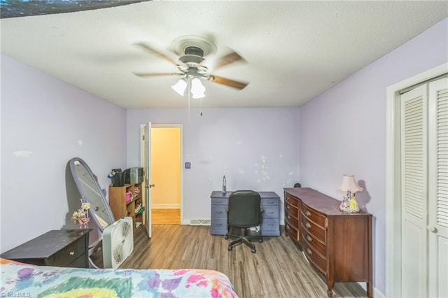 bedroom featuring wood finished floors, a desk, a ceiling fan, a closet, and baseboards