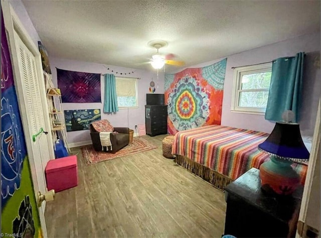 bedroom featuring wood finished floors, a textured ceiling, multiple windows, and ceiling fan