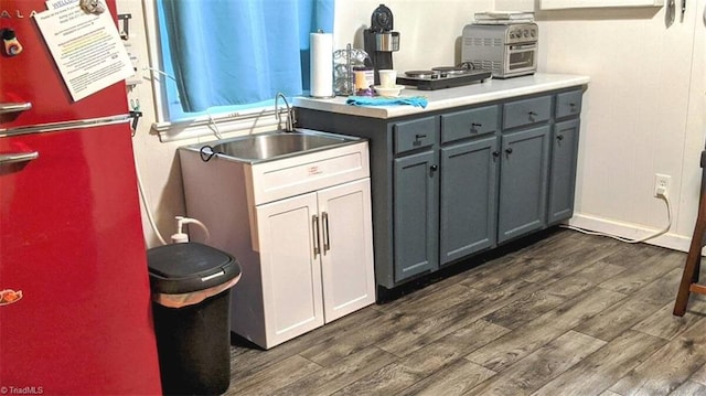 kitchen with freestanding refrigerator, a sink, gray cabinets, dark wood-style floors, and light countertops