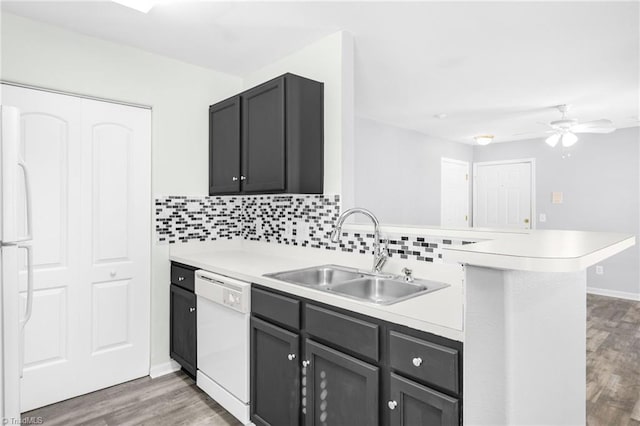 kitchen with dark wood-type flooring, sink, kitchen peninsula, white appliances, and decorative backsplash