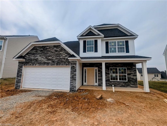 craftsman inspired home with an attached garage, covered porch, dirt driveway, and stone siding