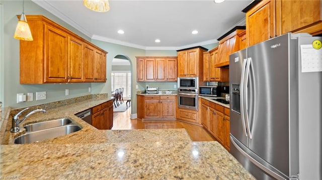 kitchen featuring light stone countertops, a sink, brown cabinets, stainless steel appliances, and ornamental molding
