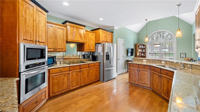 kitchen featuring light wood-type flooring, appliances with stainless steel finishes, brown cabinetry, and a sink