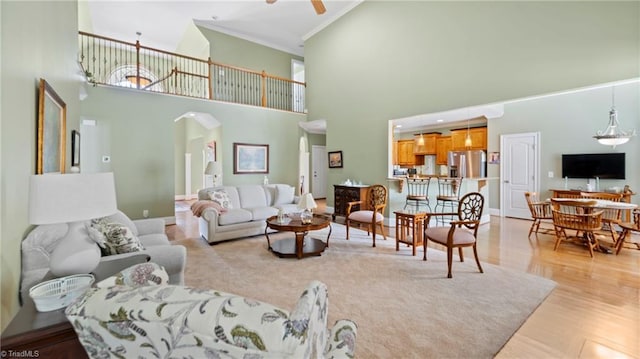 living area with a high ceiling, ceiling fan, light wood-type flooring, ornamental molding, and arched walkways