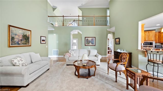 living room with visible vents, arched walkways, ornamental molding, a towering ceiling, and wood finished floors
