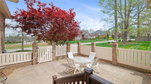 view of patio featuring fence, outdoor dining space, a gate, and a residential view