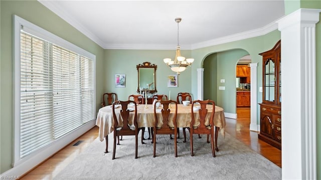dining room with light wood finished floors, a chandelier, visible vents, ornamental molding, and arched walkways