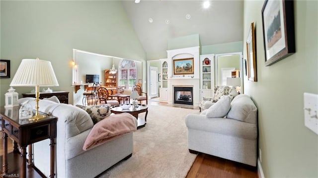 living area with a glass covered fireplace, wood finished floors, and high vaulted ceiling