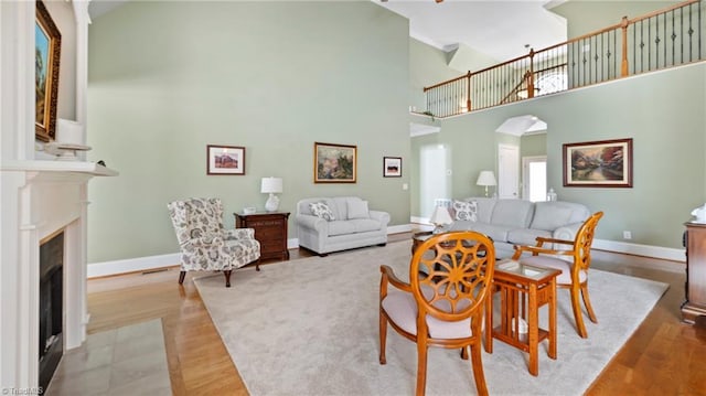 dining space featuring a fireplace with flush hearth, high vaulted ceiling, baseboards, arched walkways, and wood finished floors