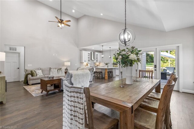 dining space with ceiling fan with notable chandelier, high vaulted ceiling, and dark hardwood / wood-style floors