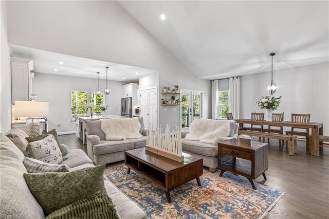 living room with high vaulted ceiling, a wealth of natural light, dark wood-type flooring, and a chandelier