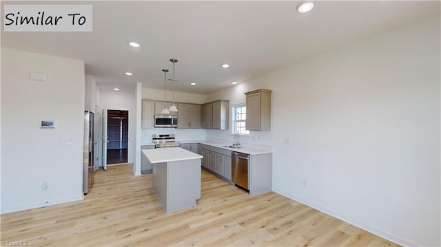 kitchen featuring light wood-style flooring, appliances with stainless steel finishes, a center island, gray cabinetry, and a sink