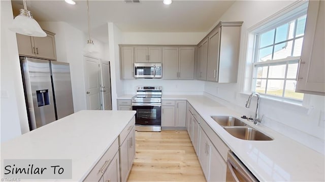 kitchen with stainless steel appliances, gray cabinetry, light wood-type flooring, pendant lighting, and a sink