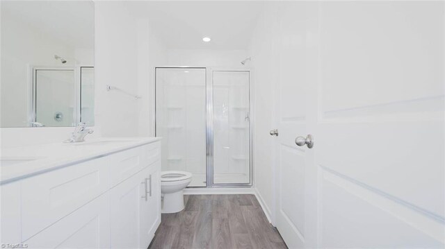 bathroom featuring hardwood / wood-style floors, vanity, toilet, and a shower with door