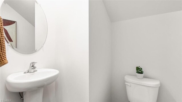 bathroom featuring toilet, lofted ceiling, and sink