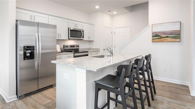 kitchen with white cabinetry, a kitchen island with sink, a breakfast bar, appliances with stainless steel finishes, and light wood-type flooring