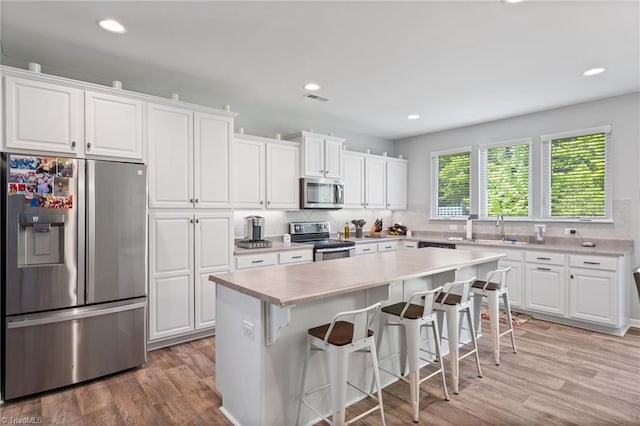 kitchen with a kitchen island, light hardwood / wood-style floors, stainless steel appliances, and white cabinetry