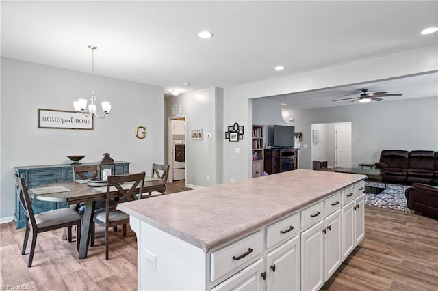 kitchen featuring a kitchen island, light hardwood / wood-style floors, ceiling fan with notable chandelier, white cabinetry, and pendant lighting