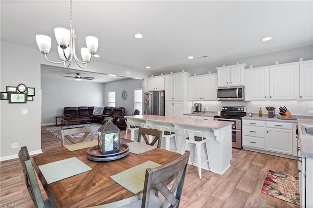 kitchen featuring appliances with stainless steel finishes, a center island, backsplash, ceiling fan with notable chandelier, and decorative light fixtures