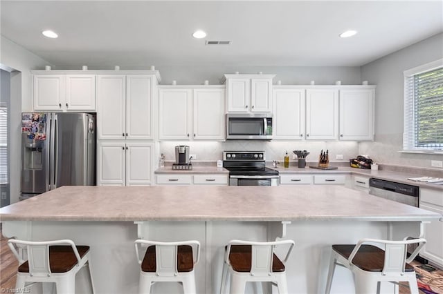 kitchen with appliances with stainless steel finishes, a kitchen island, a breakfast bar area, backsplash, and white cabinetry