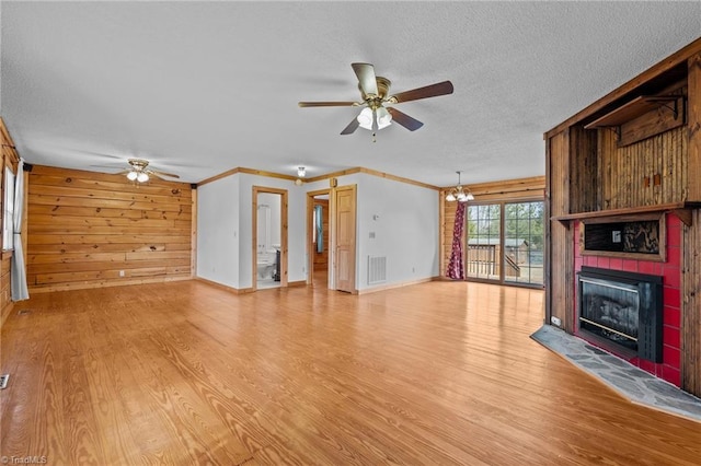 unfurnished living room featuring wooden walls, a fireplace, a textured ceiling, ceiling fan with notable chandelier, and light wood-type flooring