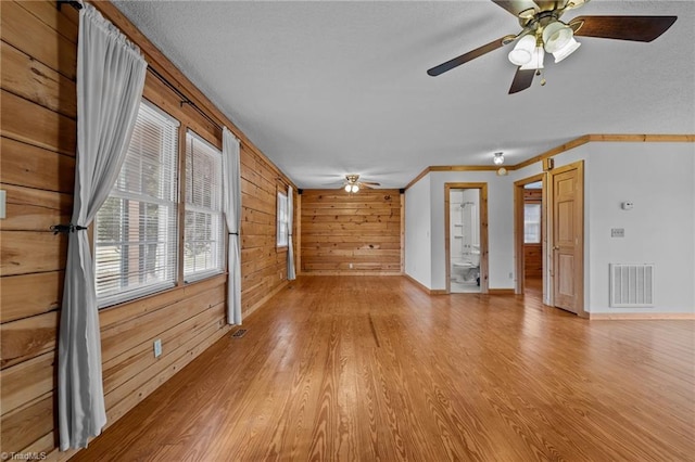 unfurnished living room featuring crown molding, ceiling fan, light hardwood / wood-style floors, and wood walls