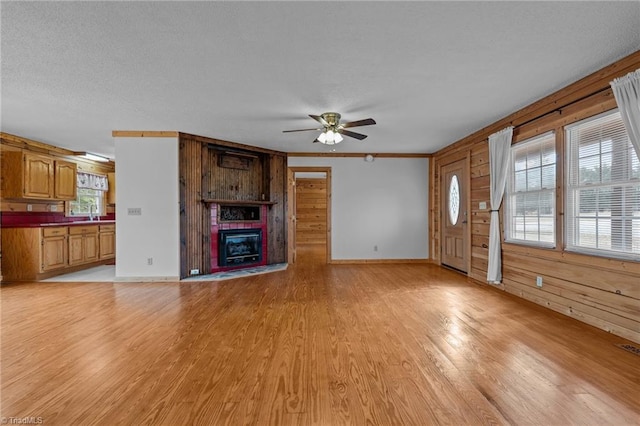 unfurnished living room featuring crown molding, light hardwood / wood-style flooring, a large fireplace, wooden walls, and ceiling fan