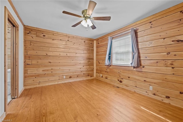 unfurnished room featuring ceiling fan, wood walls, and light wood-type flooring