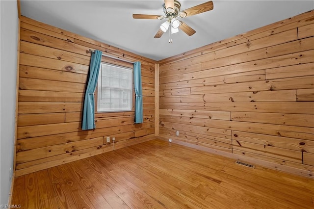 spare room featuring ceiling fan, light wood-type flooring, and wood walls