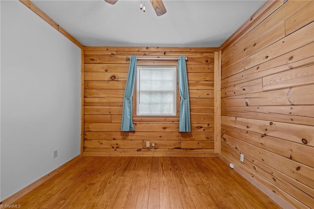 spare room featuring wood-type flooring, ceiling fan, and wooden walls