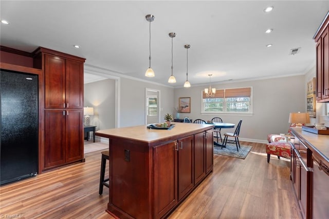 kitchen with a center island, light hardwood / wood-style flooring, black refrigerator, pendant lighting, and a breakfast bar