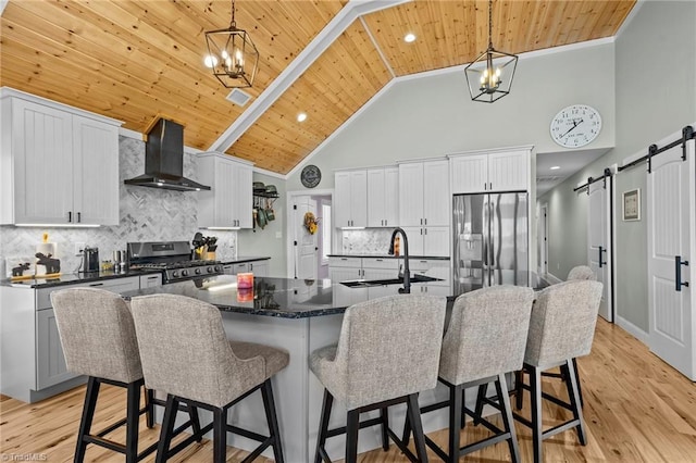 kitchen with wall chimney range hood, a barn door, backsplash, appliances with stainless steel finishes, and sink