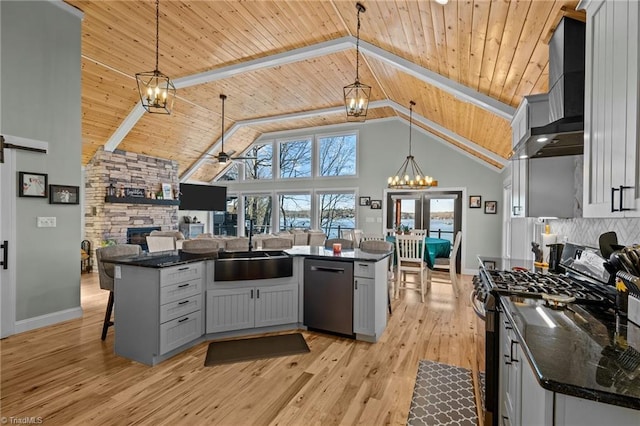 kitchen with appliances with stainless steel finishes, hanging light fixtures, high vaulted ceiling, sink, and wall chimney range hood