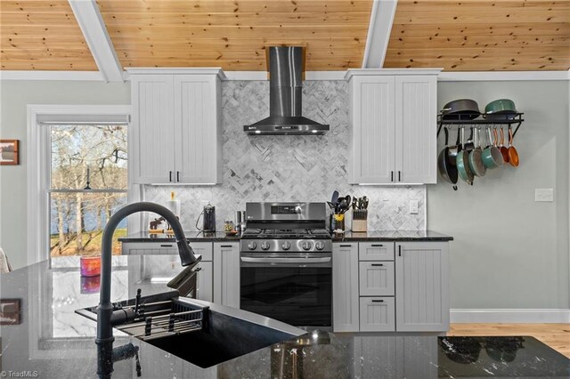 kitchen featuring gas range, wall chimney exhaust hood, white cabinetry, dark stone countertops, and wooden ceiling