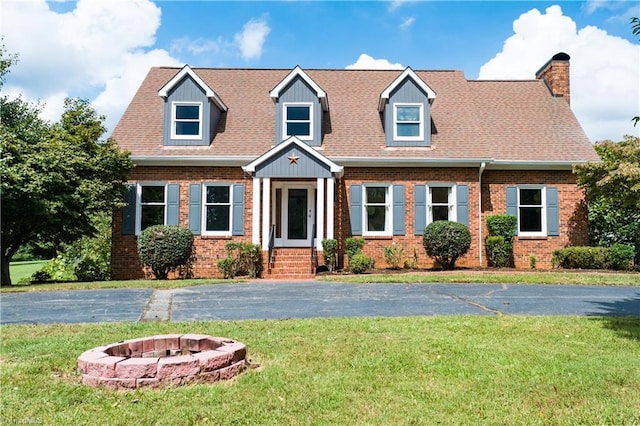 new england style home with roof with shingles, an outdoor fire pit, a front lawn, and brick siding