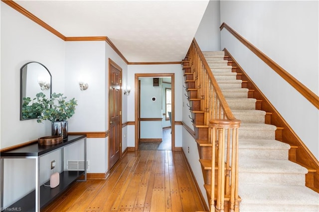 entrance foyer featuring visible vents, baseboards, stairs, ornamental molding, and light wood-type flooring